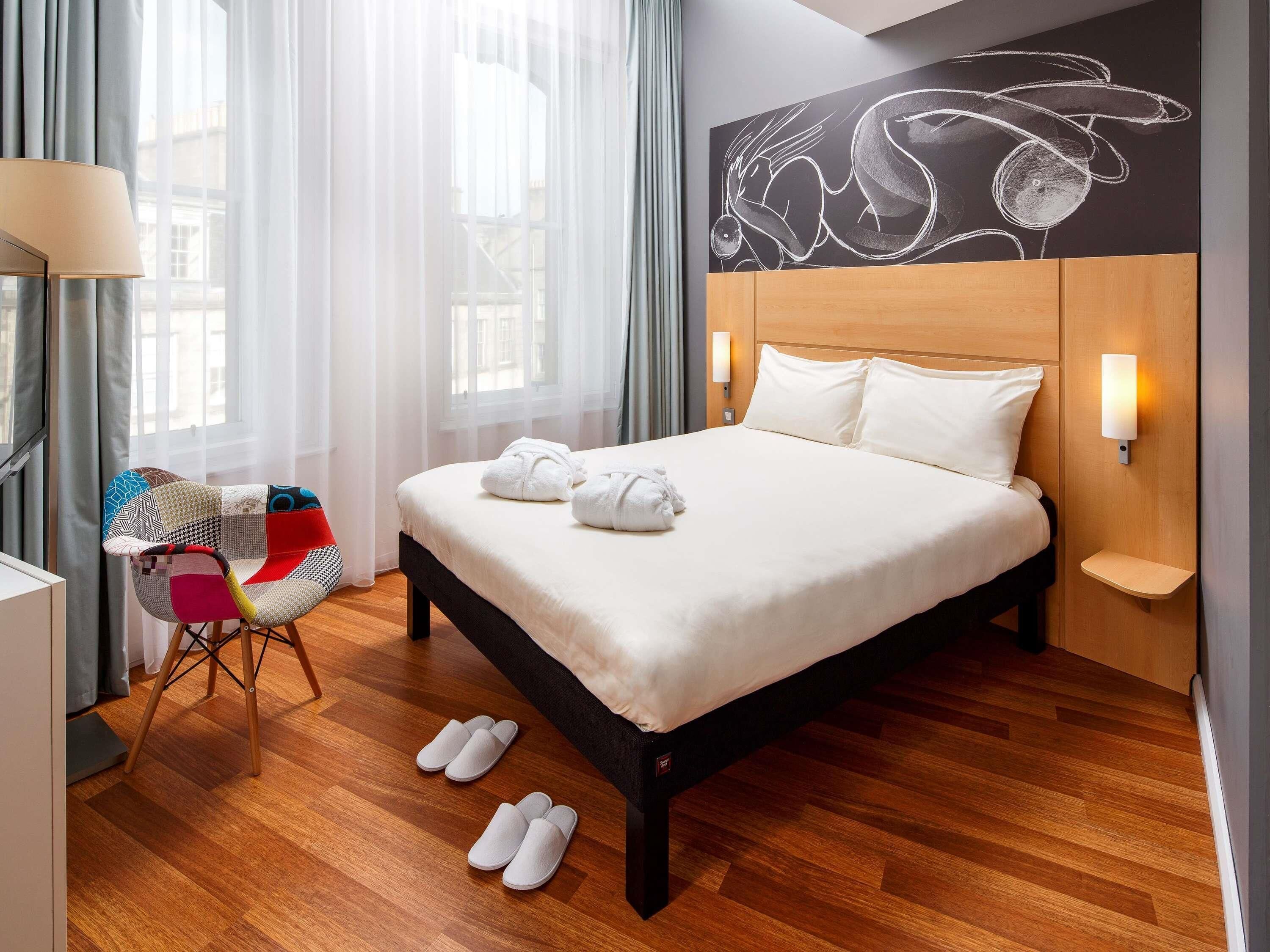 Un lit bien fait, avec du linge de lit blanc, une tête de lit en bois et un luminaire fixé au mur.