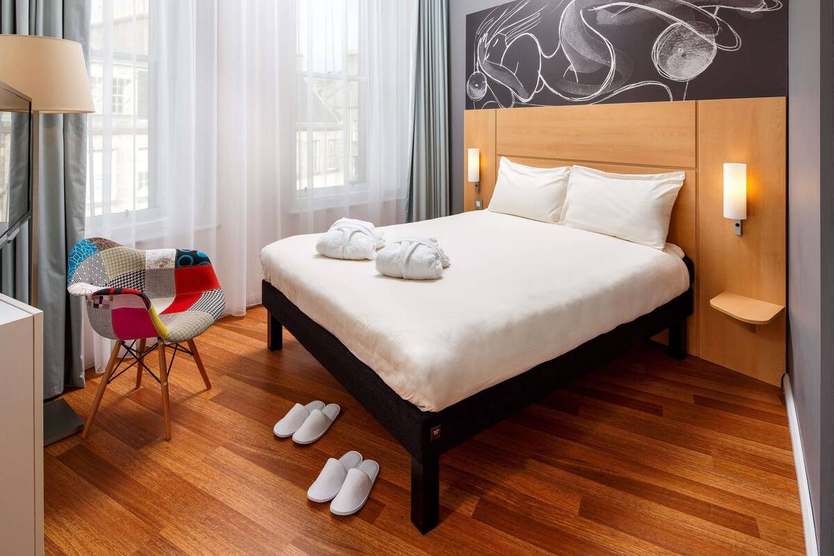 Een keurig opgemaakt bed met witte lakens, een houten hoofdbord en een wandlamp.