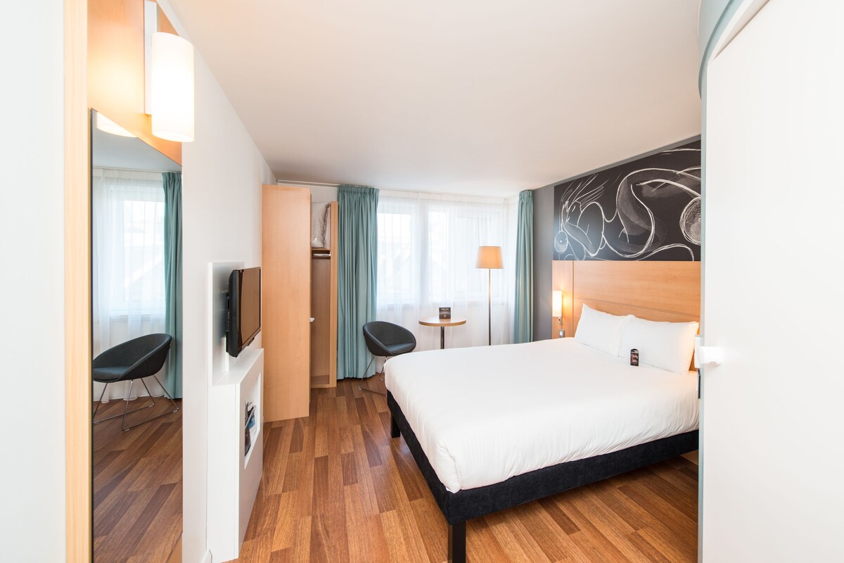 Una habitación de hotel con una cama grande, televisión, escritorio y una silla.