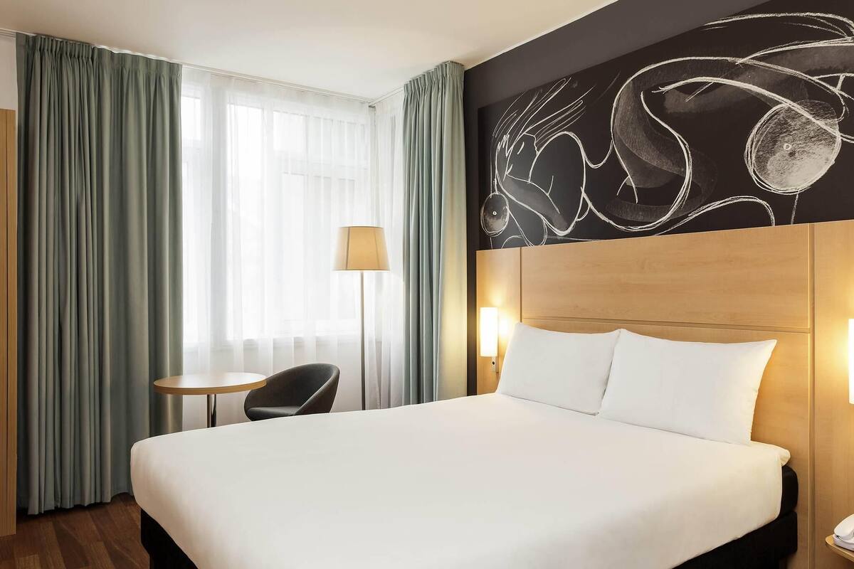 Une chambre d’hôtel avec un grand lit, une petite table, une chaise et une lampe.