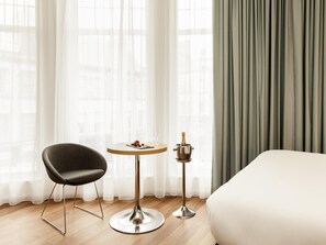 A hotel room with a bed, a round table with a bottle of champagne, a chair, and sheer curtains. - ibis Edinburgh Centre South Bridge - Royal Mile (Edinburgh)