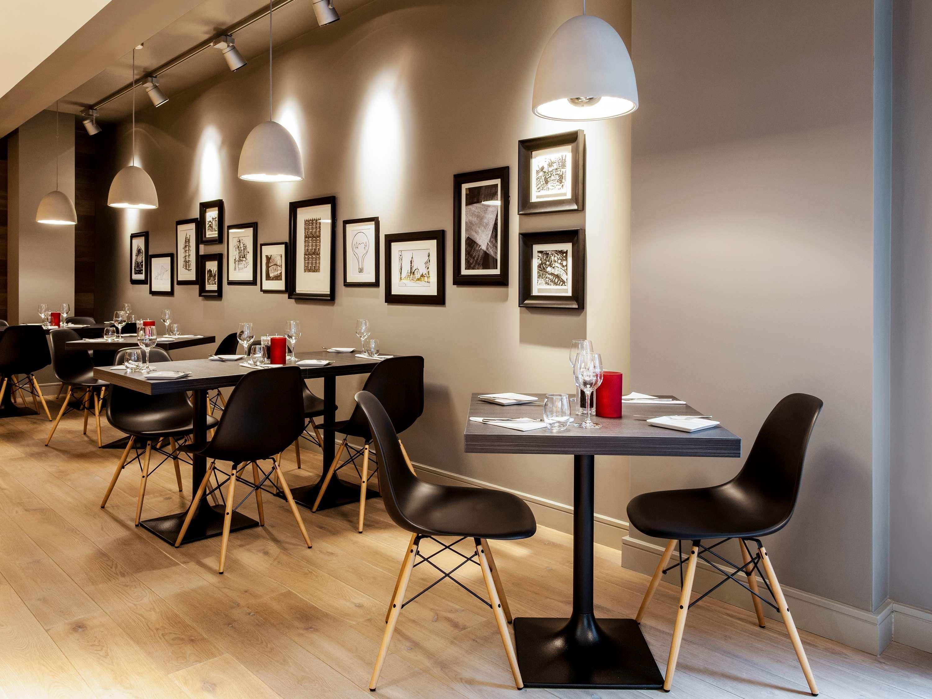 A restaurant with tables set for dining, framed artwork on the walls, and pendant lighting.