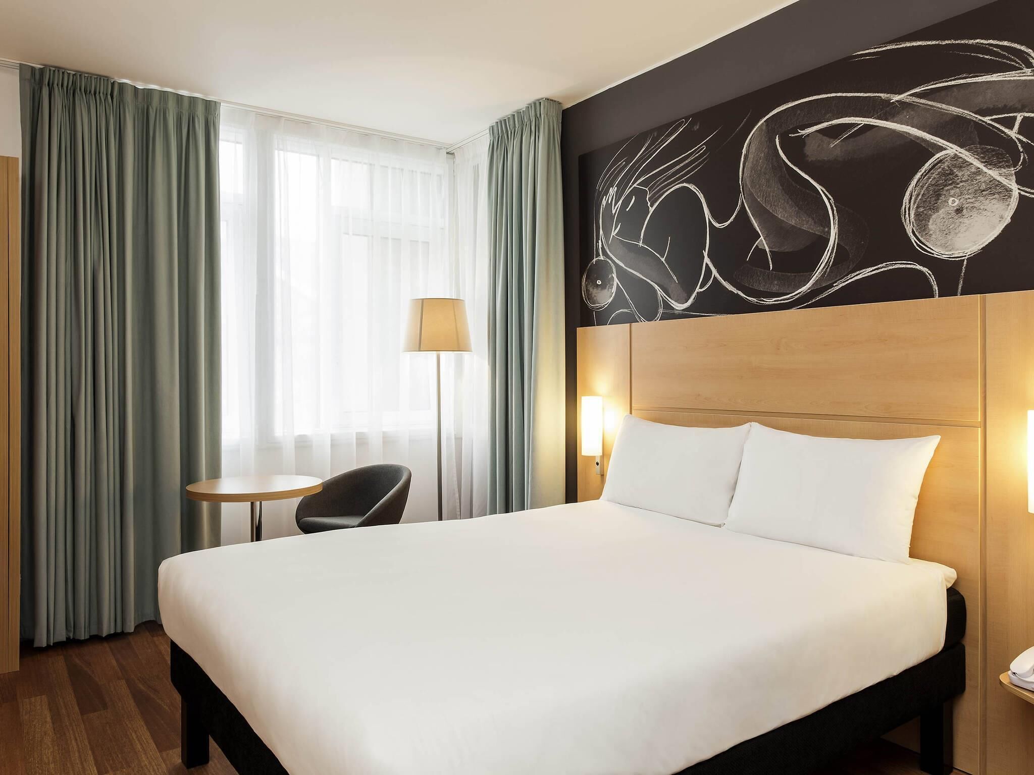 Een hotelkamer met een groot bed, een bureau, een stoel en een muur met abstracte kunst.
