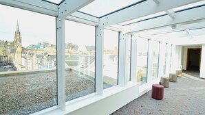 A modern interior with large windows, a patterned carpet, and a view of historic buildings.