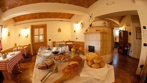 Een eetruimte met een lange tafel, gedekt voor een maaltijd, met brood, fruit en een broodmand.