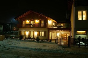 A two-story wooden building with balconies and large windows, surrounded by snow. - Agritur Renetta (Ville d'Anaunia)