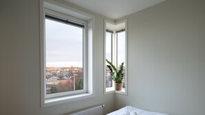 A bedroom with a large window, a radiator, and a neatly made bed with rolled towels. - Rumi Hostel (Trondheim)