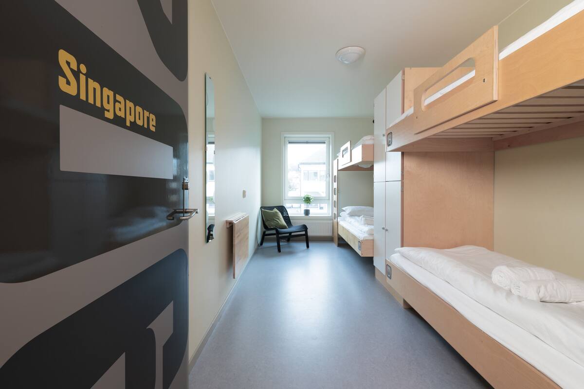 A hotel room with bunk beds, a chair, a window, and a sign reading "Singapore".