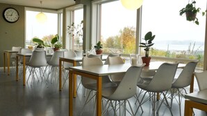 A dining area with tables and chairs, large windows with a view, and hanging plants. - Rumi Hostel (Trondheim)