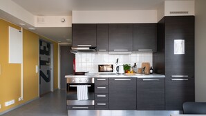 A modern kitchen with dark cabinets, a stainless steel oven, and a microwave. - Rumi Hostel (Trondheim)