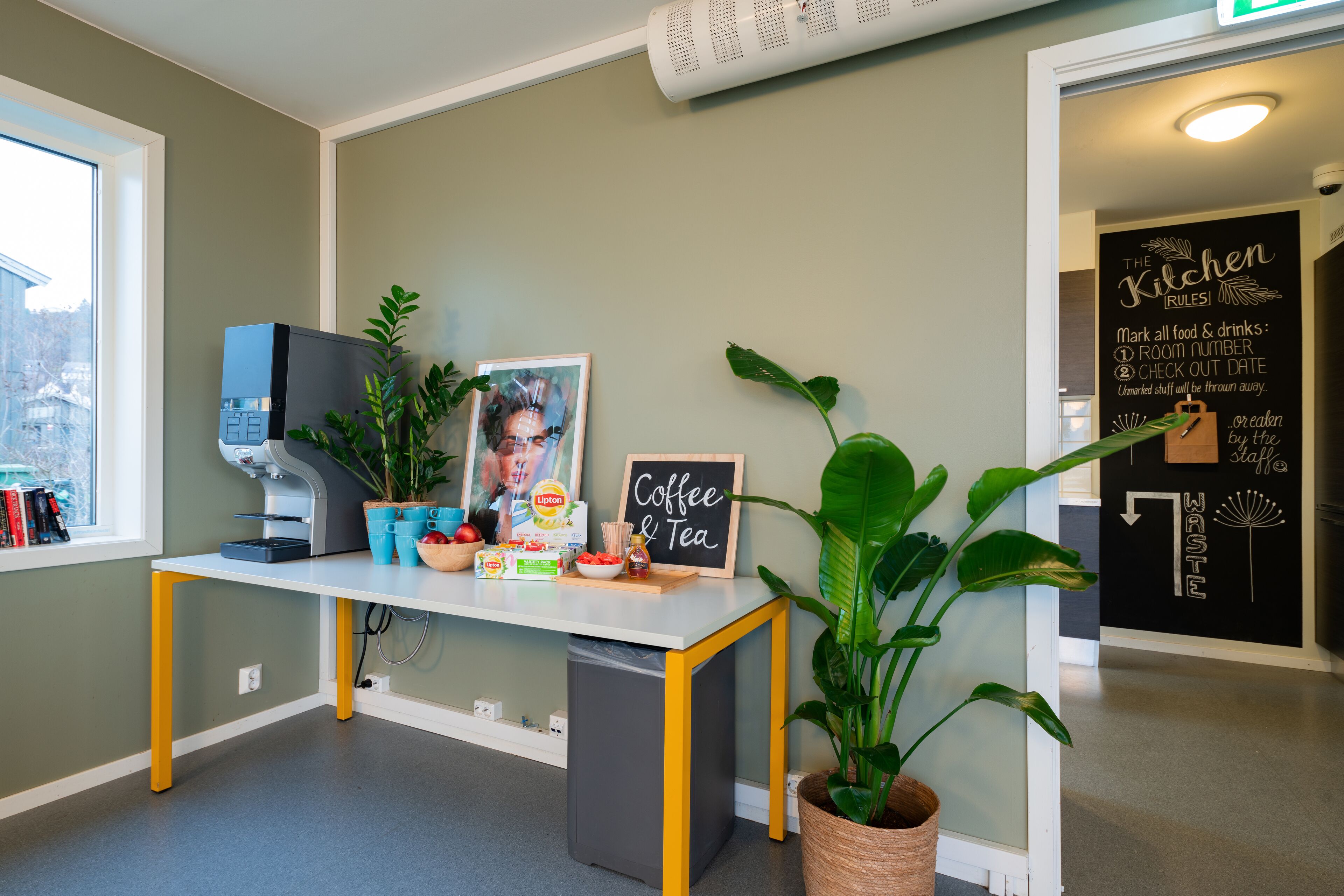 A kitchen area with a chalkboard sign reading "Coffee & Tea," a coffee machine, and a trash bin.
