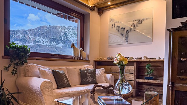 A cozy living room with a white sofa, a glass coffee table, and a view of snow-capped mountains through a large window. - Hotel da Beppe Sello (Cortina d'Ampezzo)