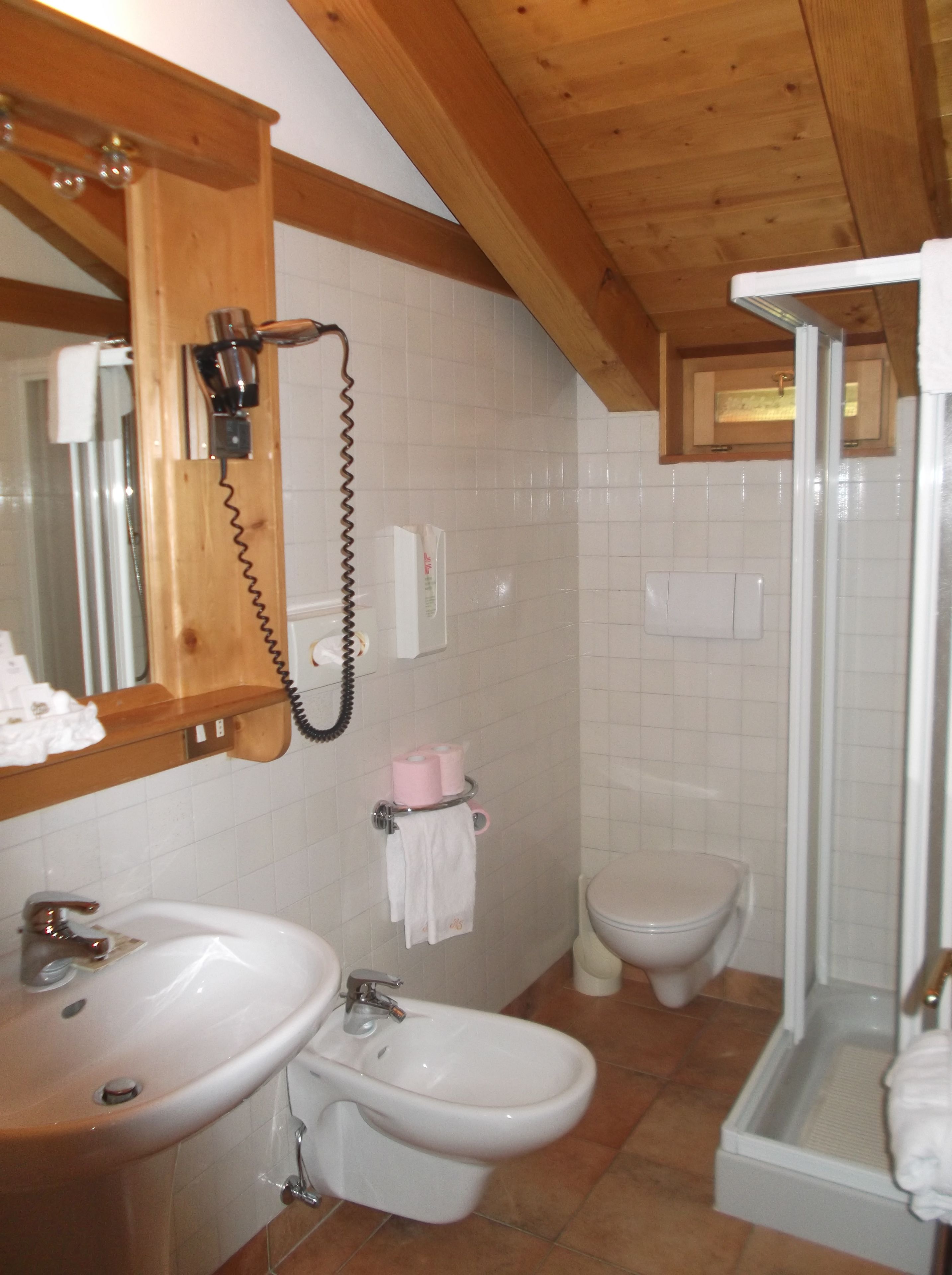 Un baño con techo de madera, lavamanos, bidé, inodoro y zona de ducha.