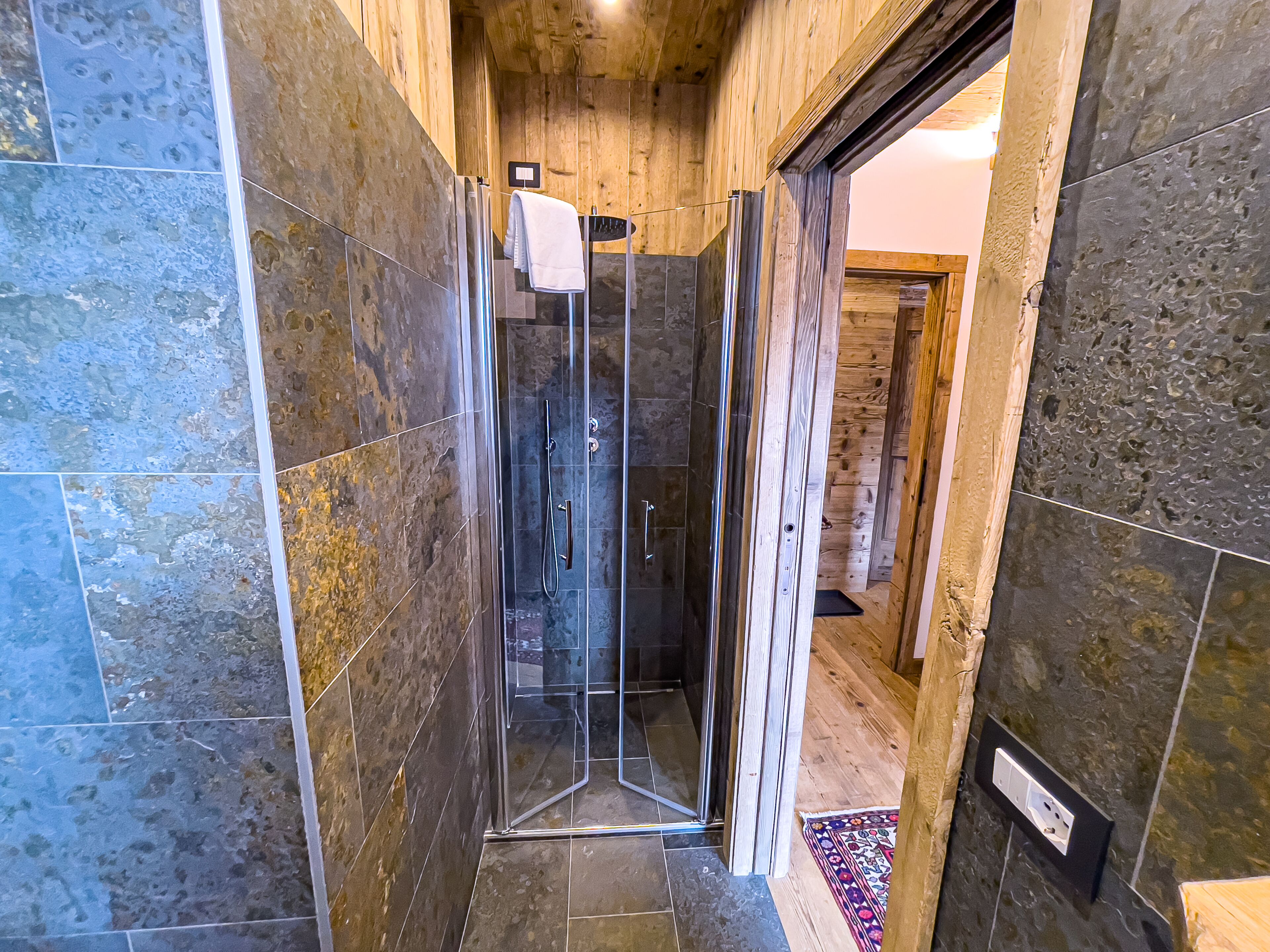 A shower area with a glass door, wooden walls, and a tiled floor.