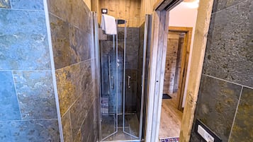 A shower area with a glass door, wooden walls, and a tiled floor.