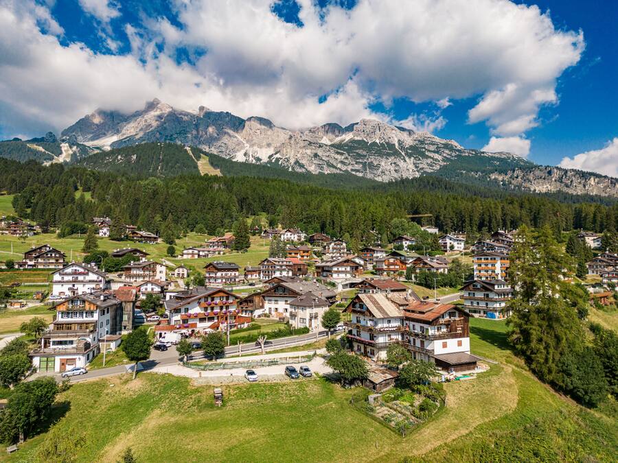 A mountain village with traditional wooden houses, a main road, and a backdrop of snow-capped peaks.