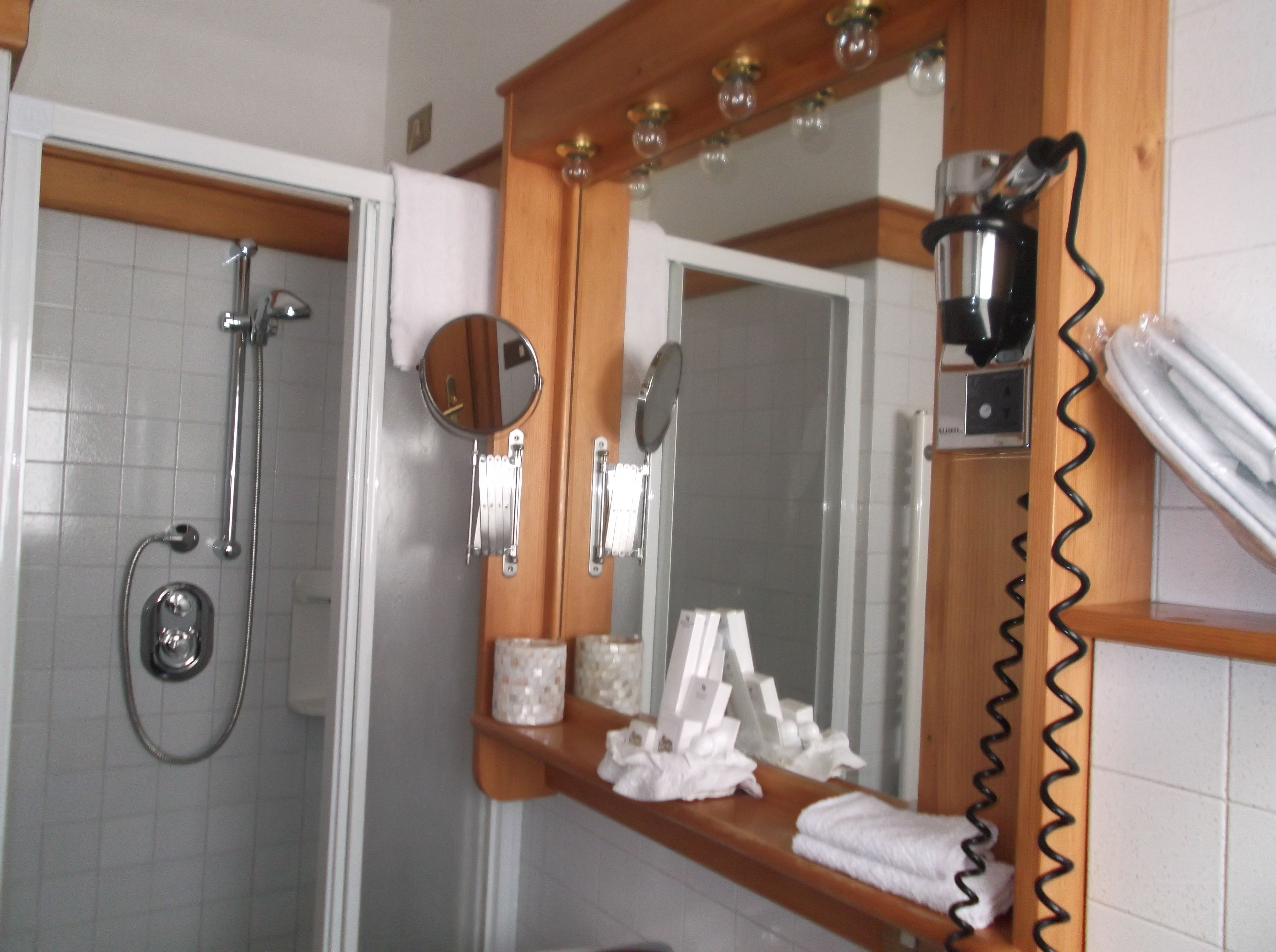 A bathroom with a shower, a mirror with a towel rack, and a hairdryer on the wall.