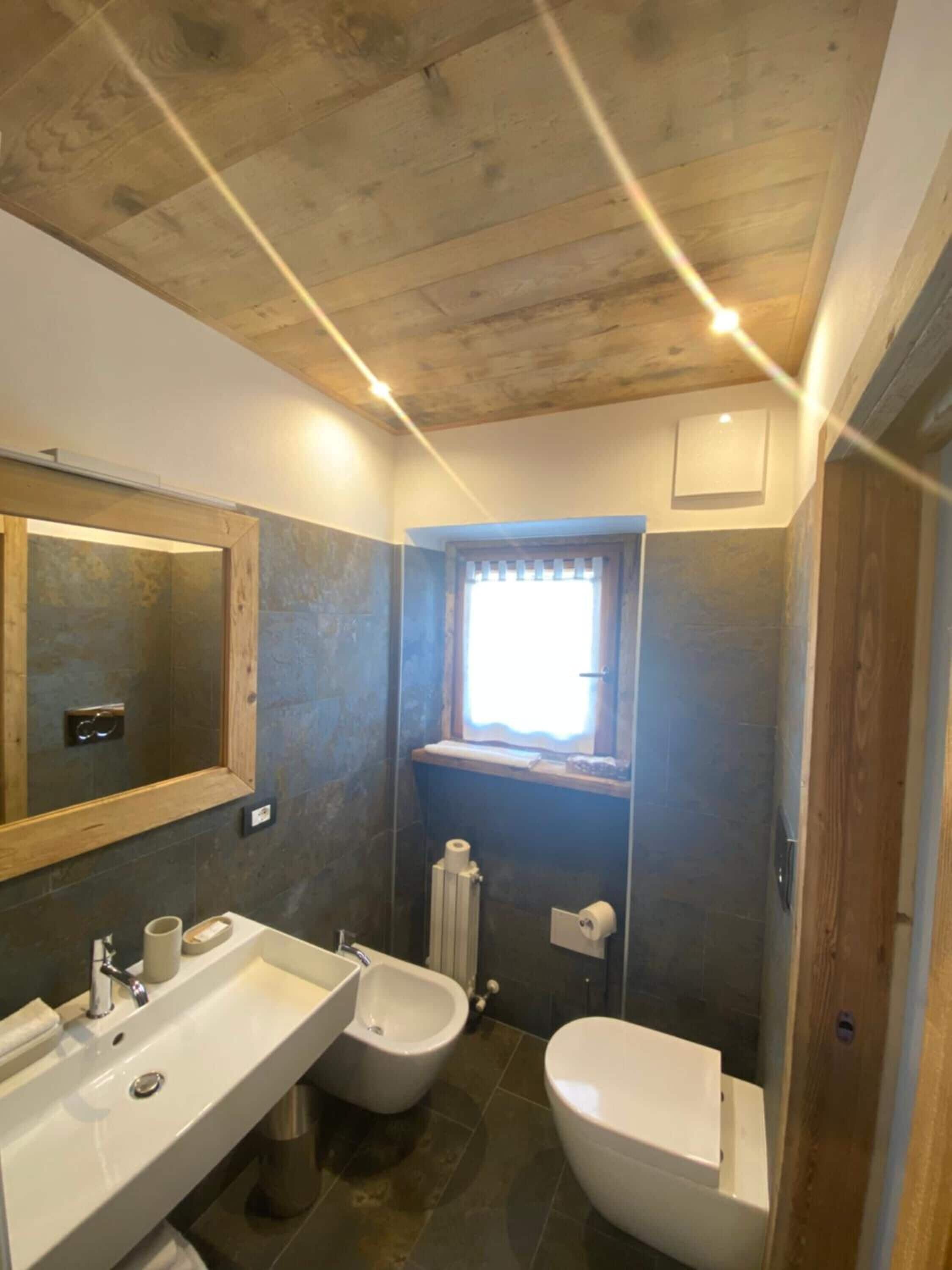 A bathroom with a wooden ceiling, two sinks, a bidet, and a toilet.