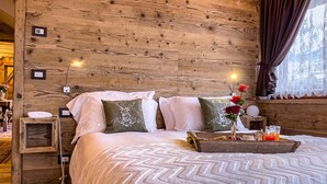 A cozy wooden room with a bed, pillows, a bedside table with a lamp, and a window with curtains. - Hotel da Beppe Sello (Cortina d'Ampezzo)