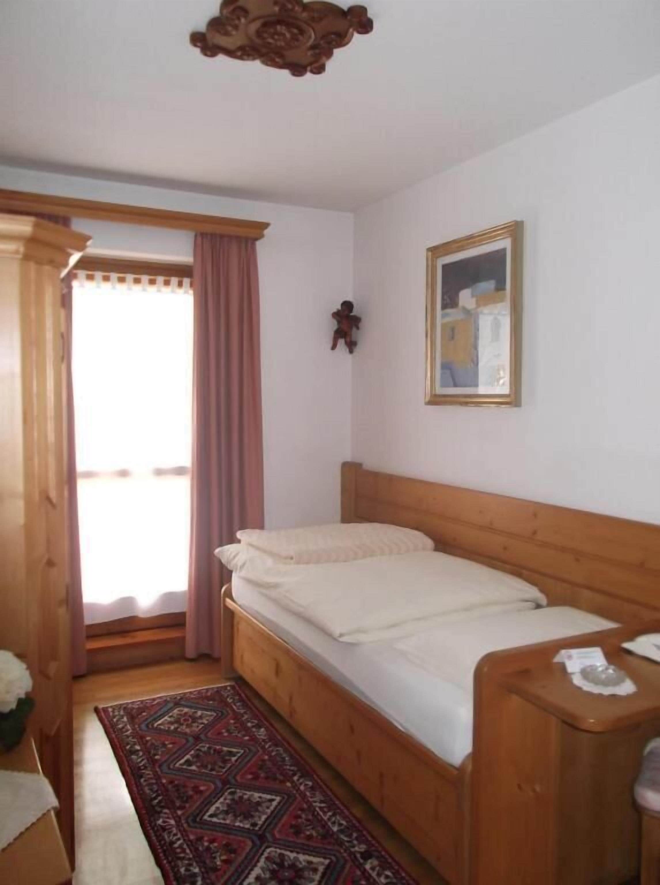 Un dormitorio con una cama de madera, una mesita de noche pequeña, un cuadro enmarcado en la pared y una alfombra estampada en el suelo.