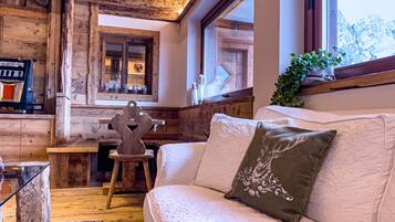 Une pièce chaleureuse avec un plafond en bois, un canapé blanc agrémenté d’un coussin vert, une table en bois et une fenêtre donnant sur des arbres.