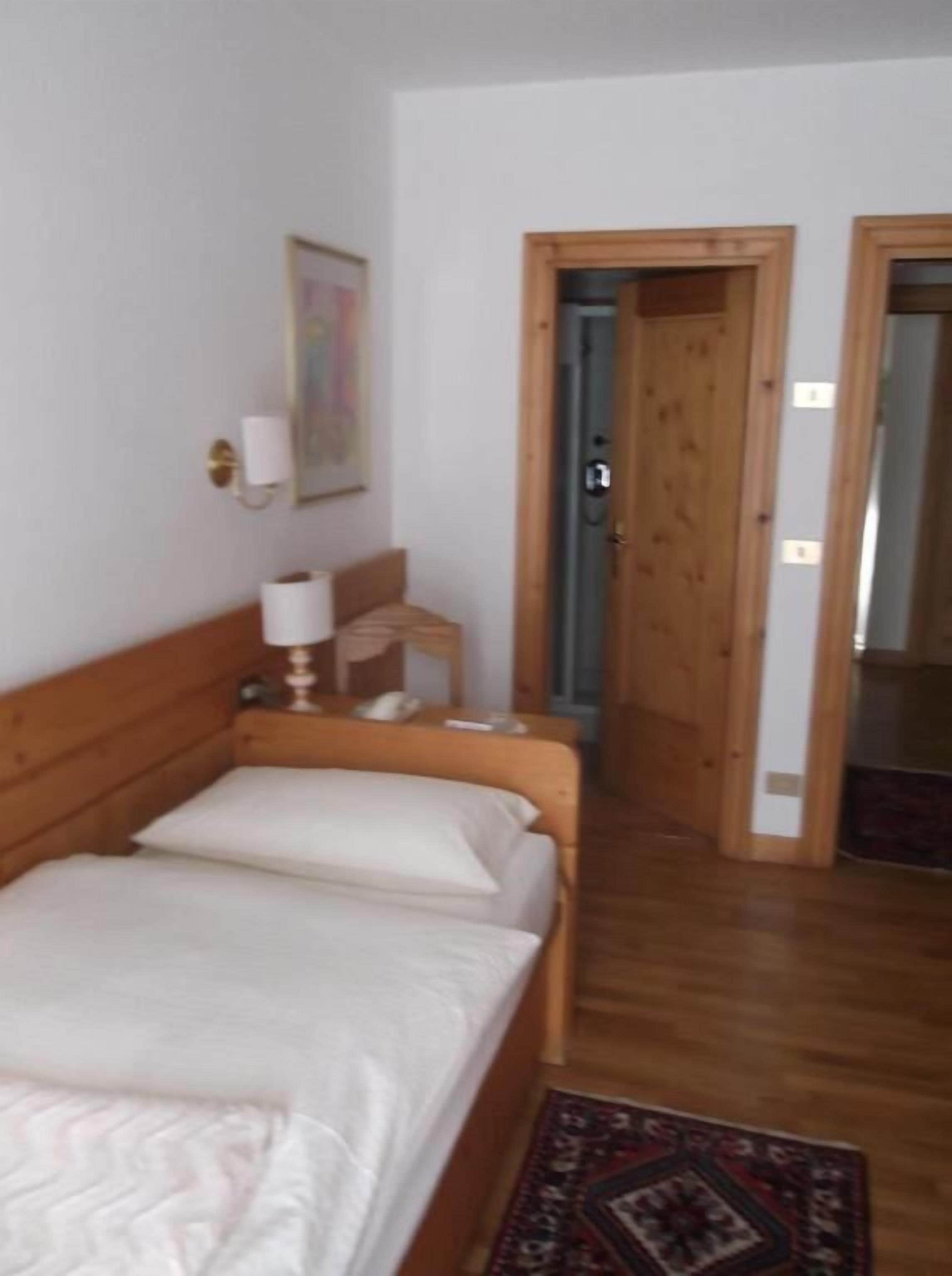 Un dormitorio con una cama de madera, una mesita de noche con lámpara y una puerta que da a otra habitación.