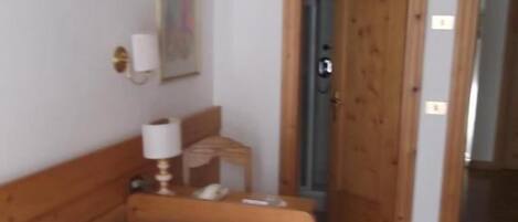 Un dormitorio con una cama de madera, una mesita de noche con lámpara y una puerta que da a otra habitación.