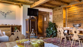 A cozy room with wooden walls and ceiling, a large painting, a television, a wooden cabinet, and a dining area with a table and chairs.