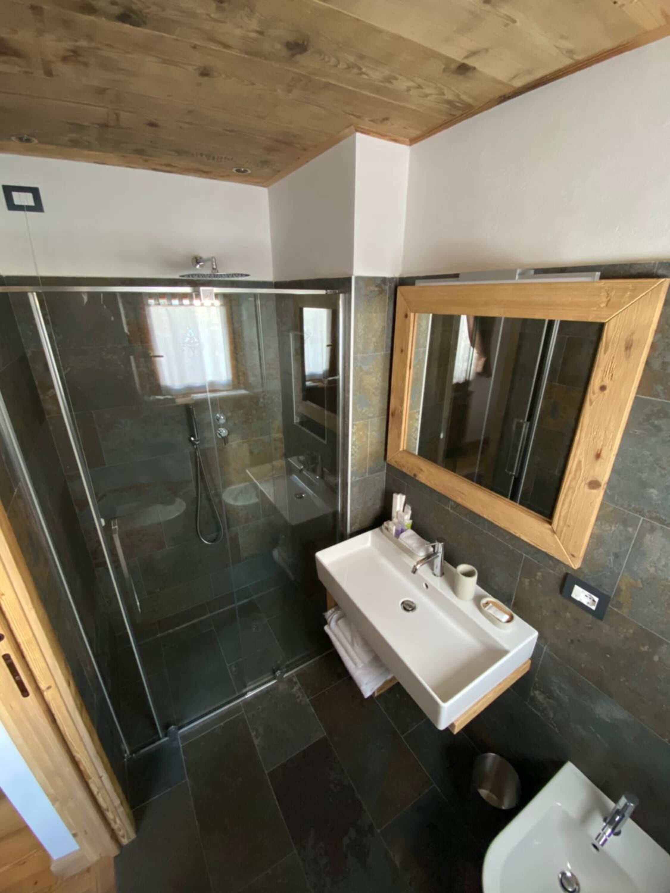 Un baño moderno con ducha de vidrio, lavamanos blanco y espejo con marco de madera.