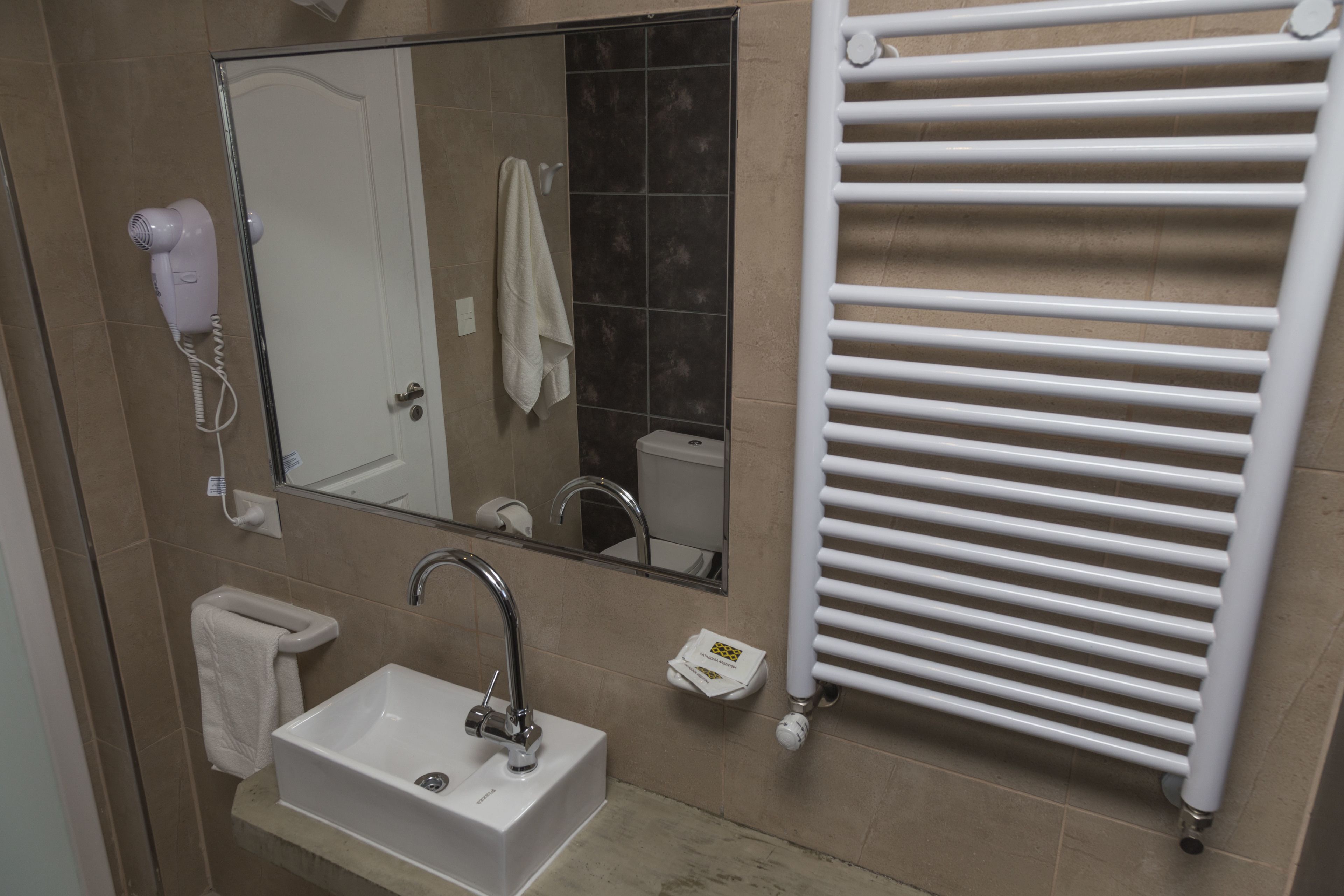 A bathroom with a white sink, a mirror, a hair dryer, a towel rack, and a white towel.