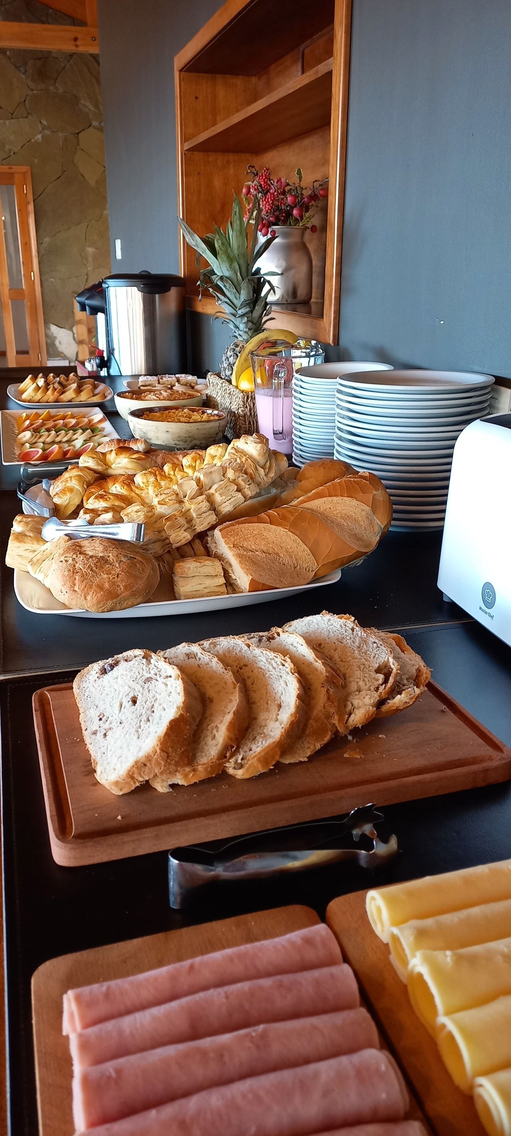 A buffet table with various food items including bread, pastries, and a fruit bowl.