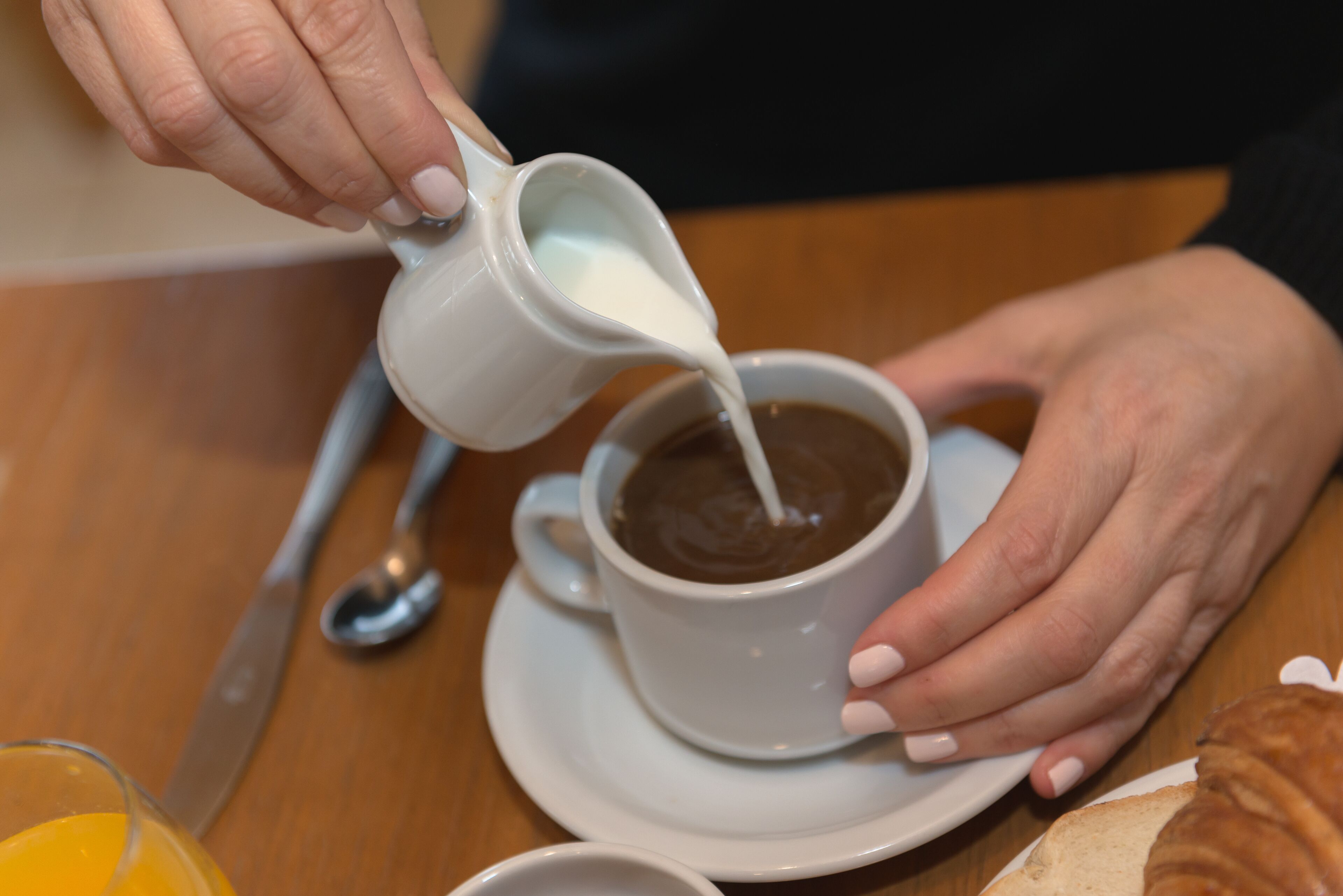 Una persona vertiendo leche en una taza de café sobre una mesa con un cuchillo y una cuchara.