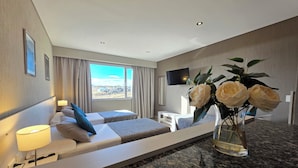 Una habitación de hotel moderna con cama, mesita de noche, lámpara y un gran ventanal con vistas.