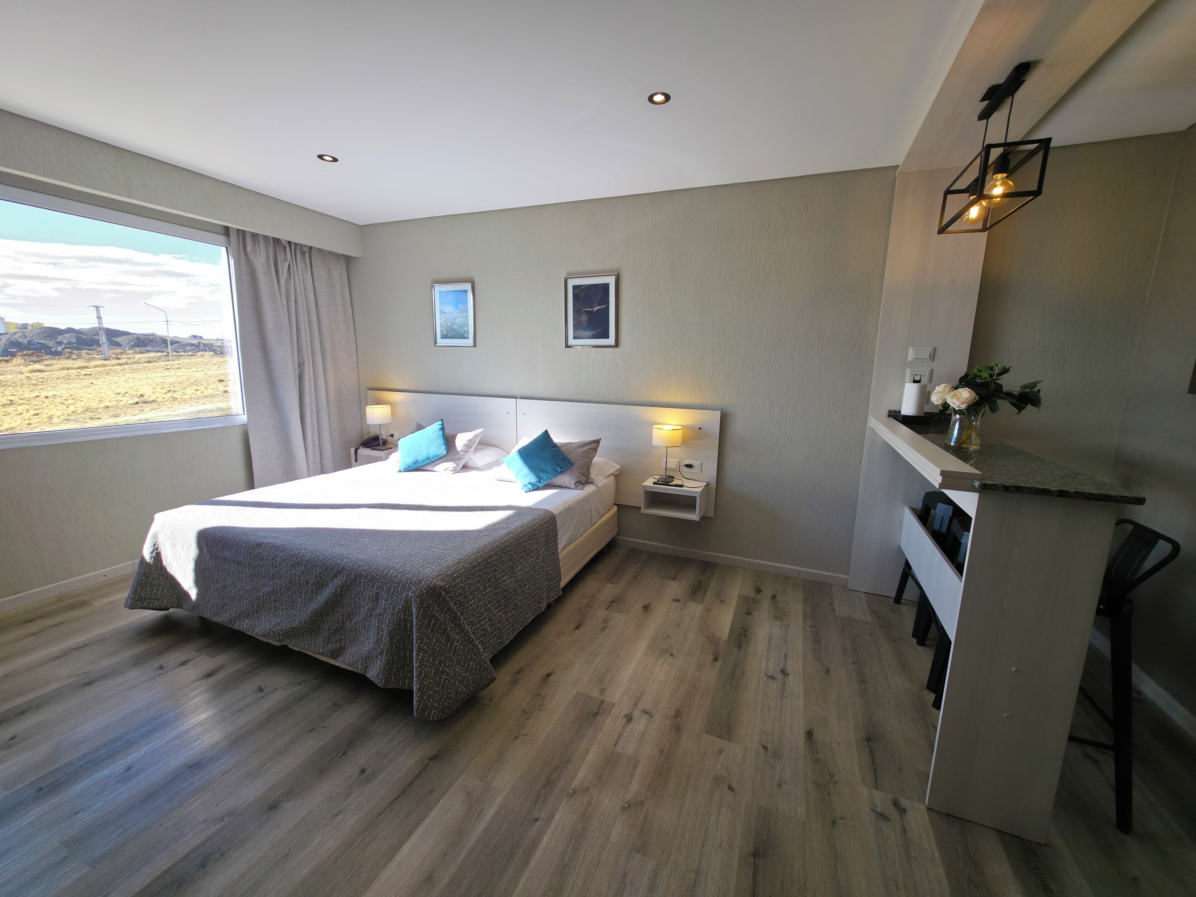 A modern hotel room with a large bed, bedside tables, a desk, and a view of the outdoors.