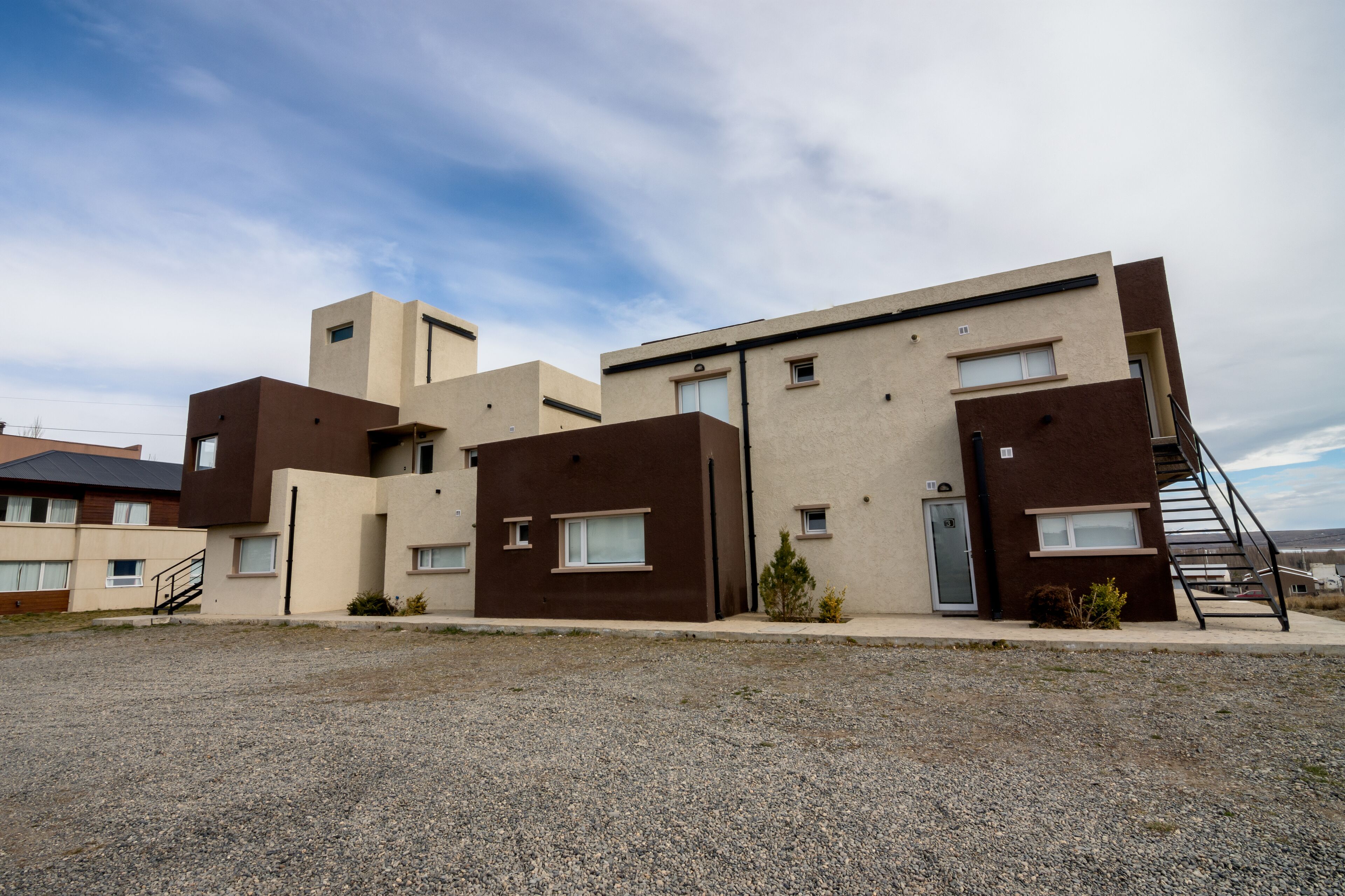 A modern building with multiple units, a gravel driveway, and a clear sky.