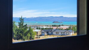 Vista a través de una ventana de una zona costera con cielo despejado, montañas al fondo y una pequeña isla.