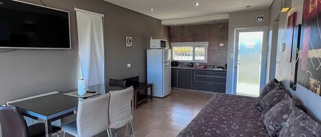 Una habitación de hotel moderna con una cama grande, un escritorio con silla, televisor y kitchenette.