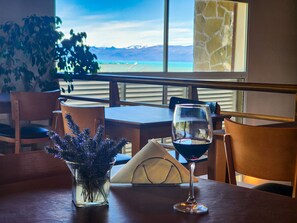 A table with a wine glass and a vase of flowers, overlooking a scenic view through large windows. - Tierra Tehuelche (El Calafate)