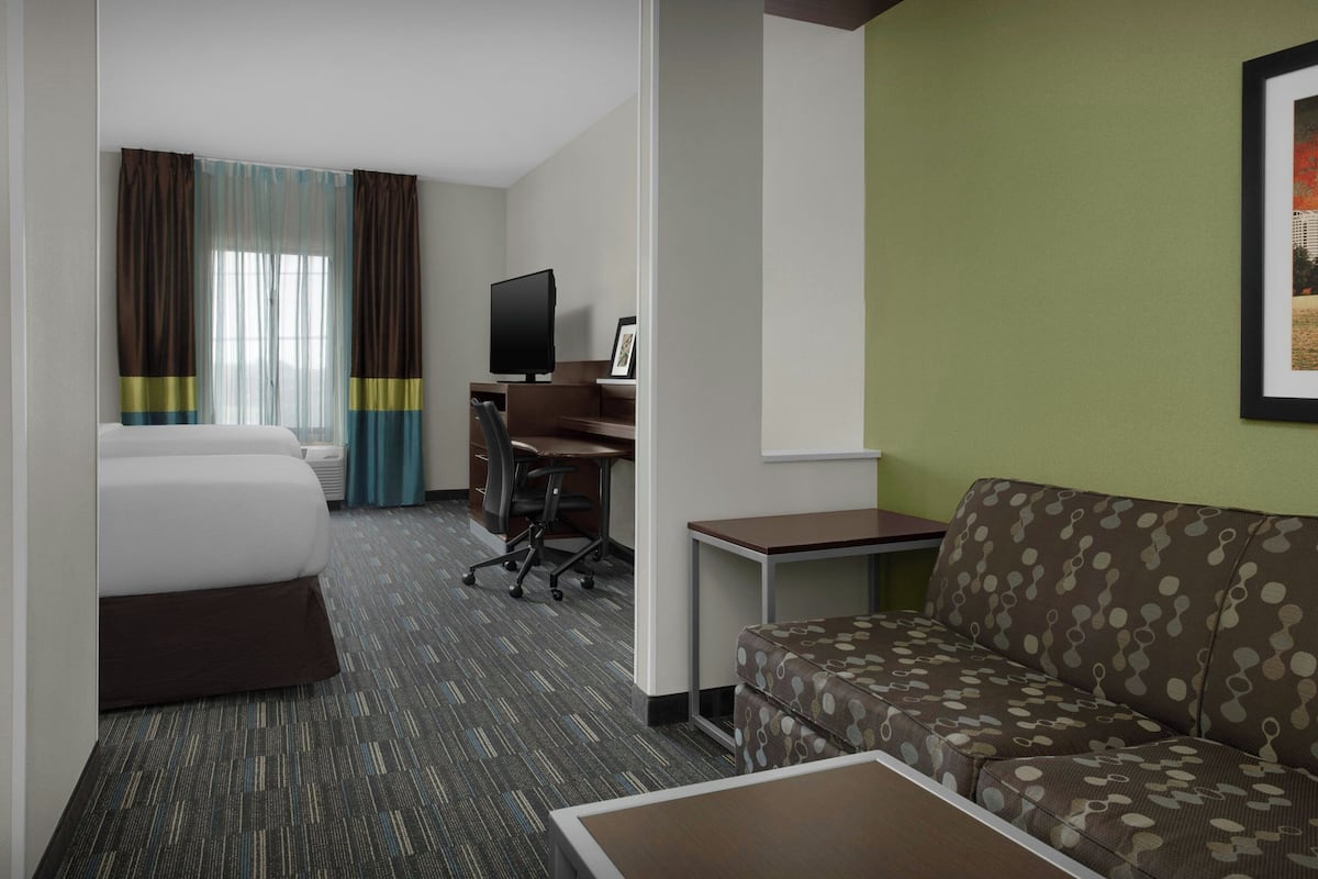 A hotel room with a bed, a desk with a computer, a sofa, and a television.
