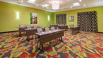 Une salle de conférence aux murs verts, dotée d’un tapis à motifs et de plusieurs tables entourées de chaises, ainsi que de bouteilles d’eau.