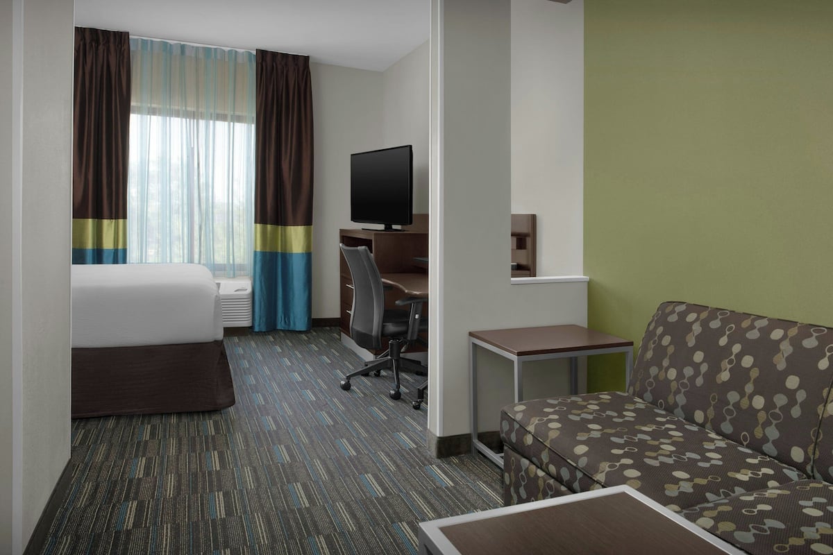 A hotel room with a bed, a desk with a computer, a TV, a sofa, and a small table.