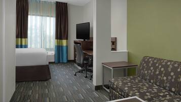 Habitación de hotel con cama, escritorio con computadora, televisor, sofá y una mesita.