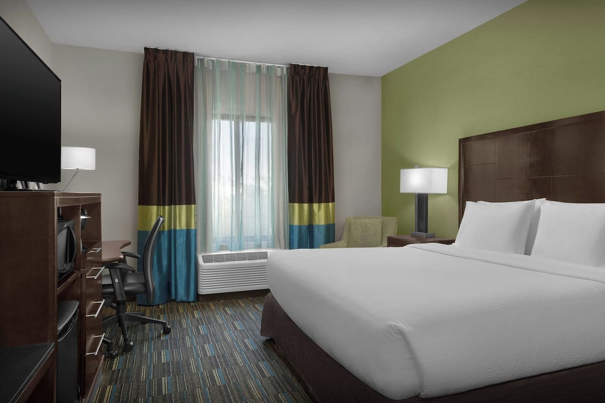 A hotel room with a large bed, a desk with a chair, a television, and a window with curtains.
