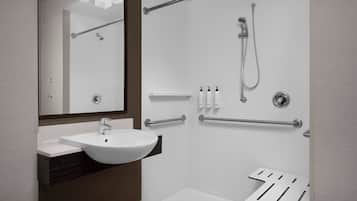 A modern bathroom with a white sink, a mirror, a shower, and a toilet with grab bars.