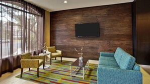 A modern living room with a sofa, two armchairs, a coffee table, and a TV mounted on a wooden wall. - Fairfield Inn & Suites by Marriott Austin Northwest/Research Blvd (Austin)