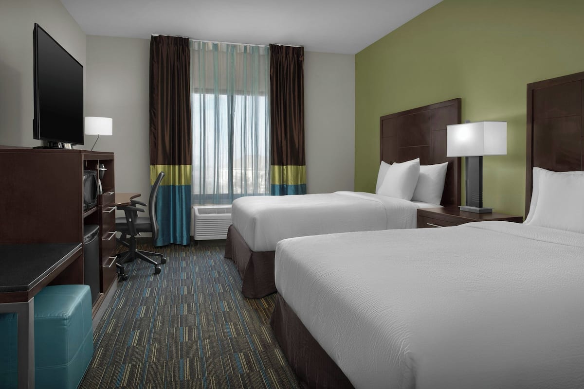 A hotel room with two beds, a desk with a chair, a TV, and a window with curtains.