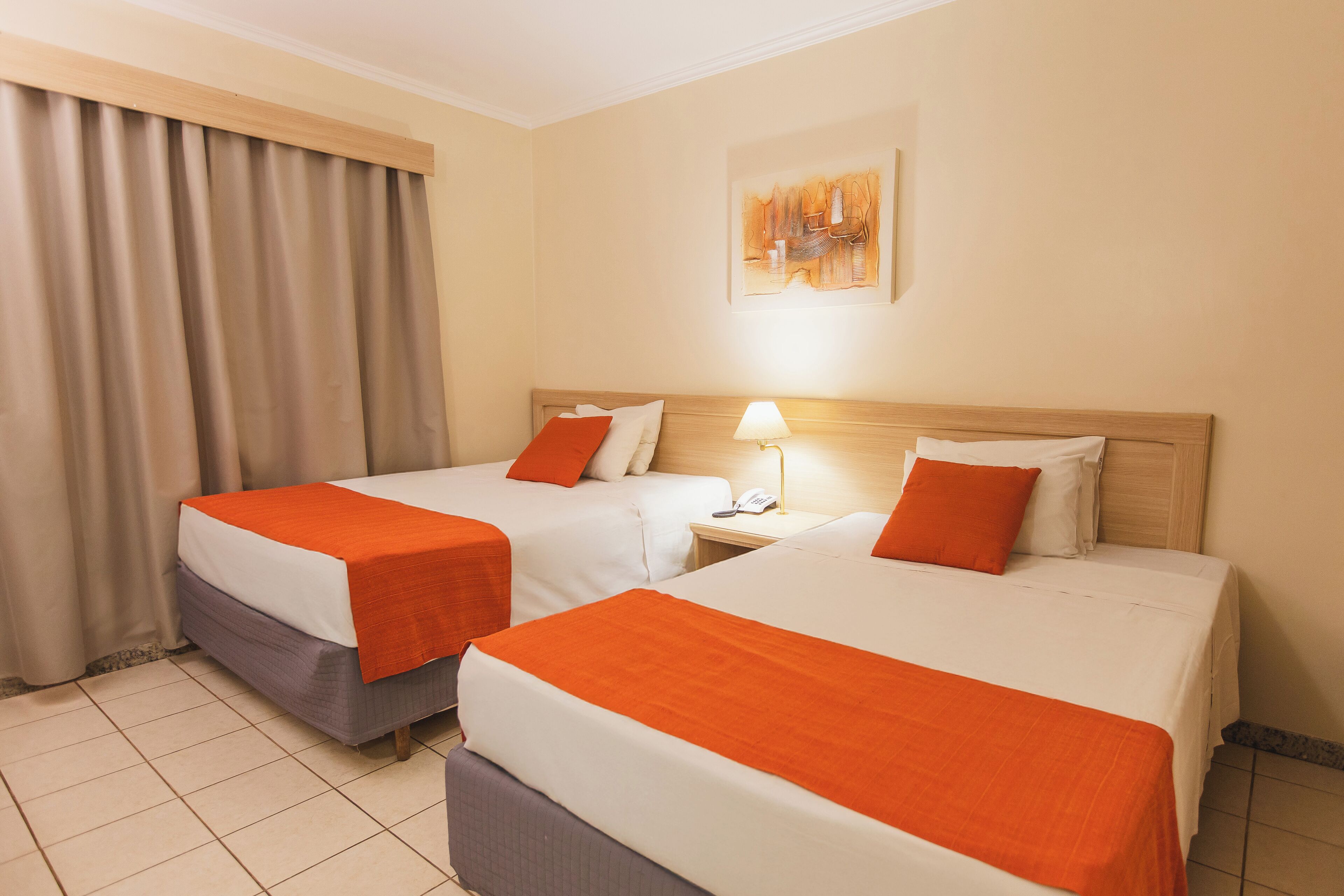 Een hotelkamer met twee bedden, elk met een oranje deken, een nachtkastje met een lamp en een schilderij aan de muur.