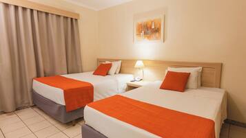 A hotel room with two beds, each with an orange blanket, a nightstand with a lamp, and a painting on the wall.