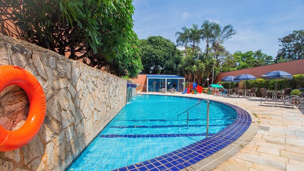 Una piscina con muro de piedra y borde de azulejos azules, rodeada de sillas de descanso y sombrillas.