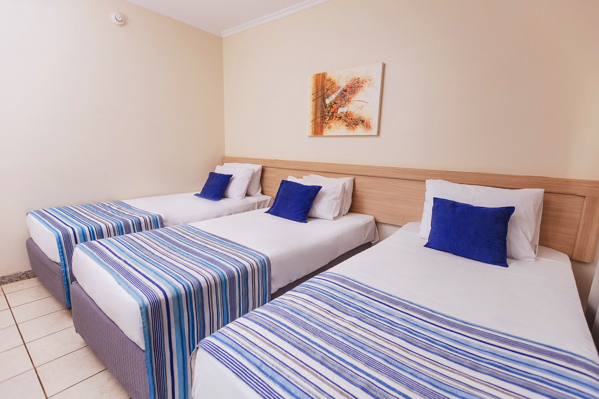 A hotel room with three single beds, each with a striped bedspread and a blue pillow.